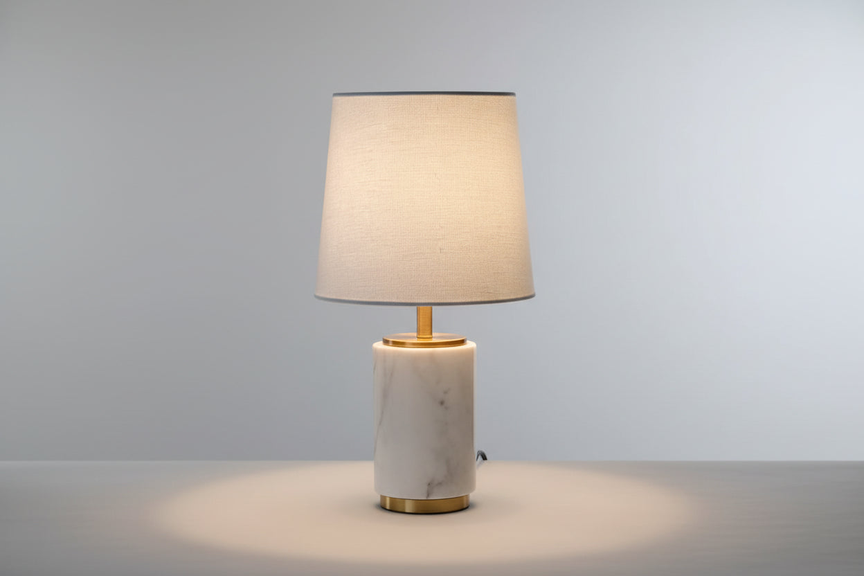 A small white lamp with a marble base and a gold-colored metal stem, providing a warm light glow.